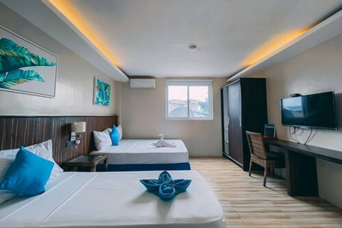 A hotel room with two beds, a desk, a television, and a window.