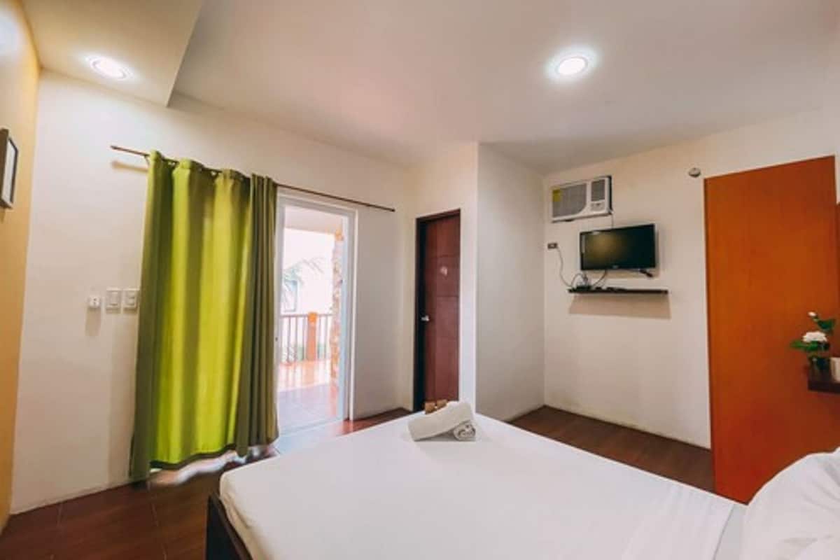 A hotel room with a bed, a television mounted on the wall, a door, and a window with curtains.