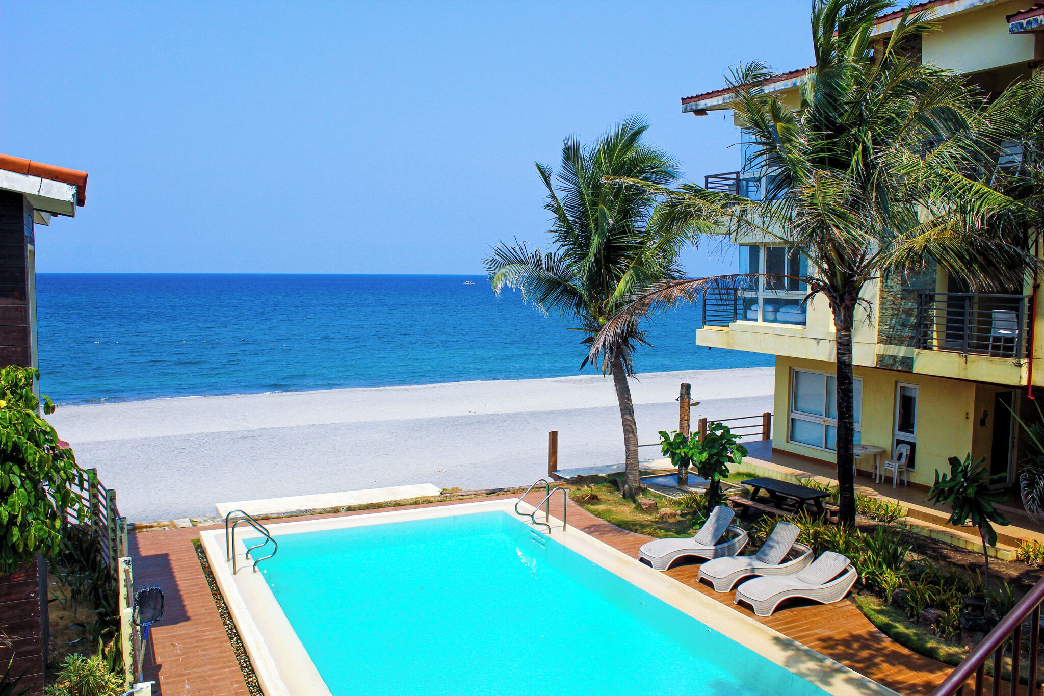 A pool with lounge chairs, a beach view, and a building with balconies.