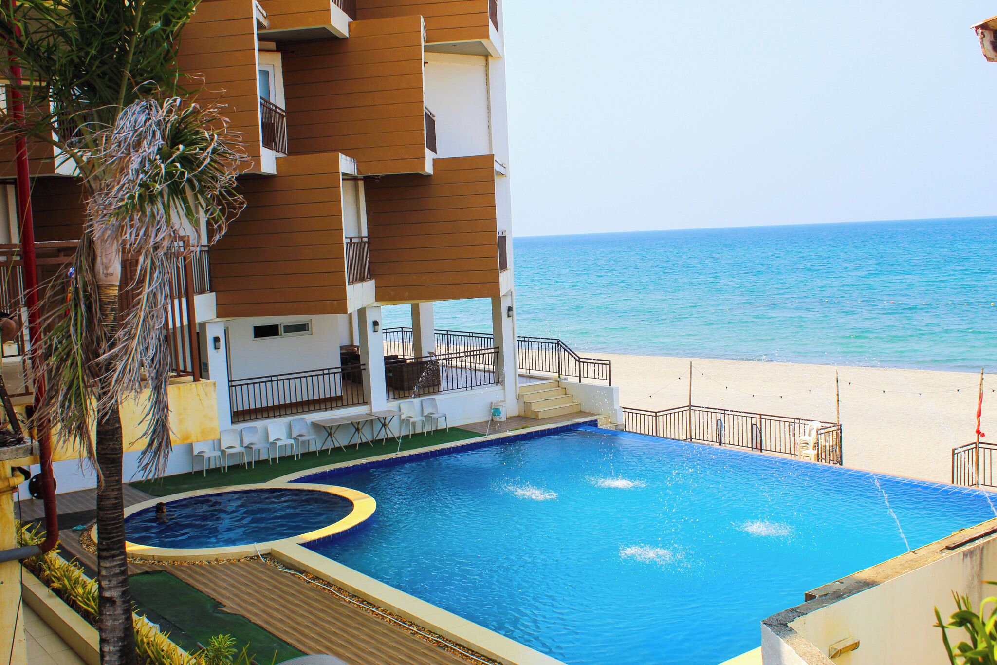 Una piscina con vistas a la playa y al océano, rodeada por un edificio de varios pisos con balcones.