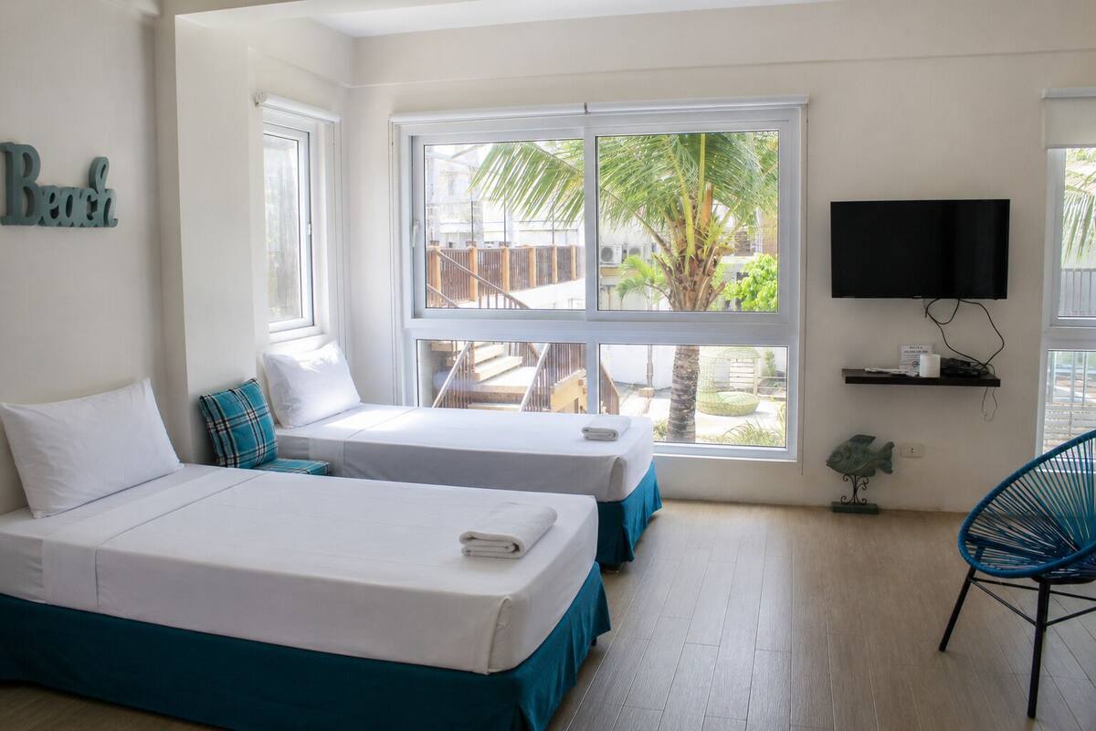 A hotel room with two beds, large windows, a TV, and a chair.