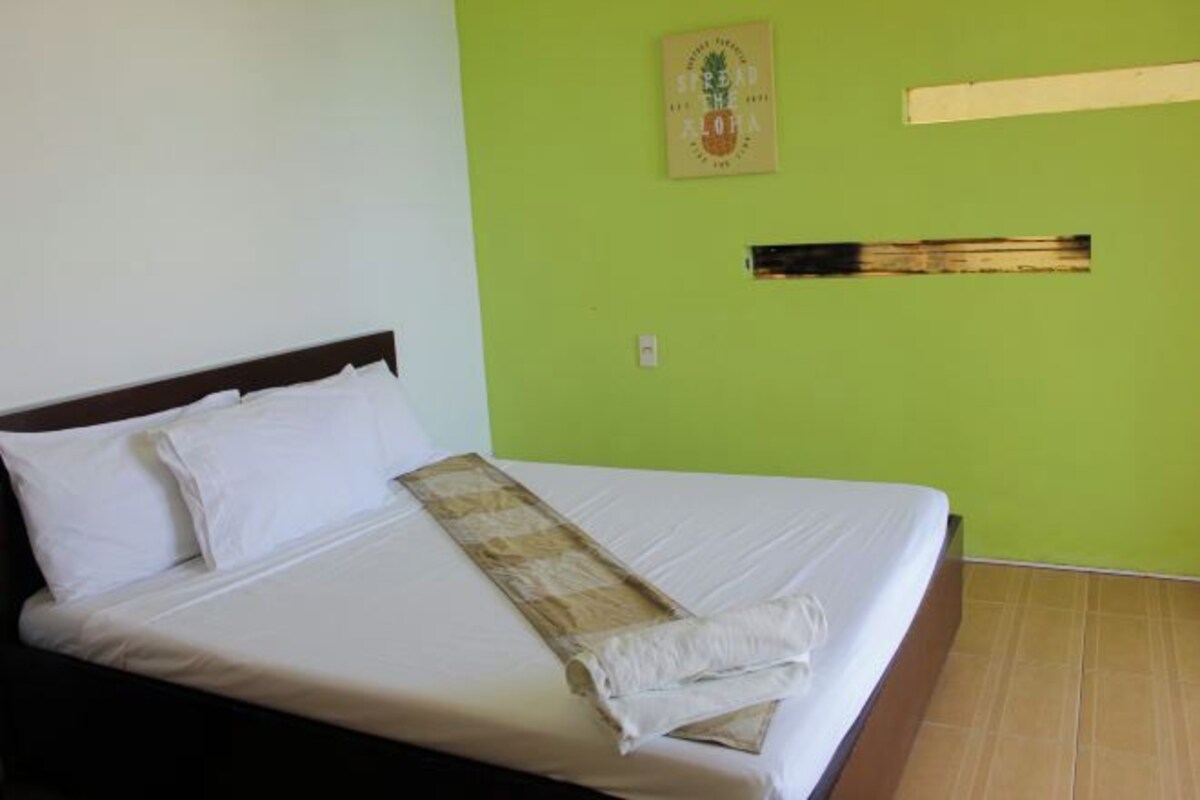 A bed with white linens, a wooden headboard, and a green wall with a framed picture.