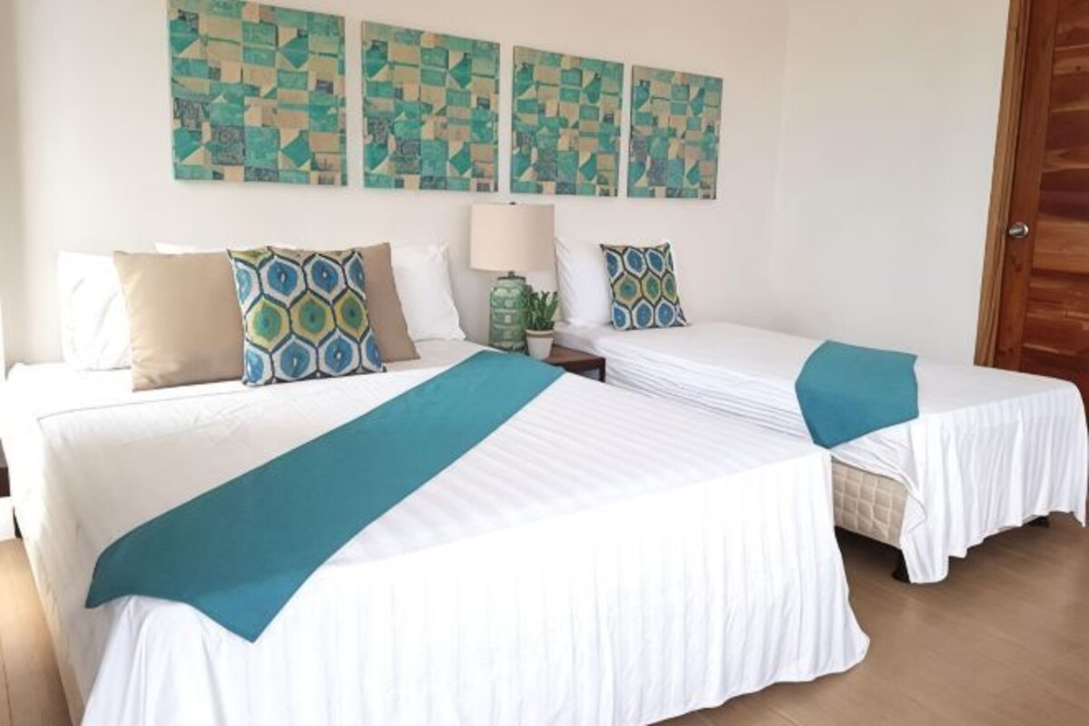 A hotel room with two beds, a nightstand, a lamp, and abstract wall art.