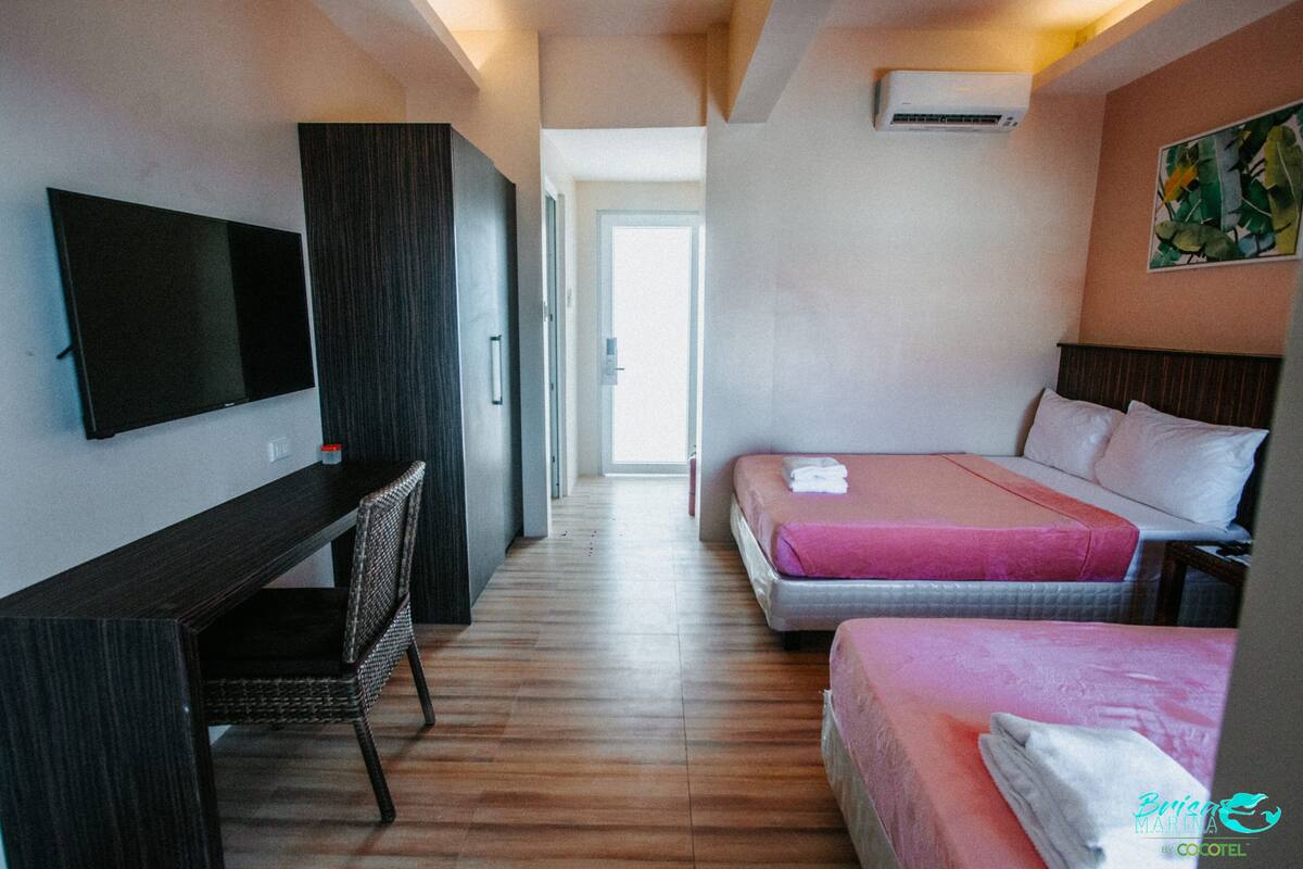 A hotel room with a flat-screen TV, a desk, two beds with pink bedding, and a painting on the wall.