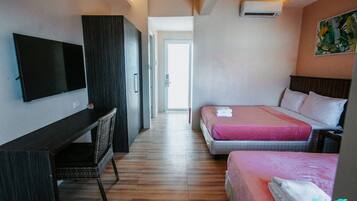 Habitación de hotel con televisión de pantalla plana, escritorio, dos camas con ropa de cama rosa y un cuadro en la pared.