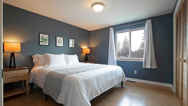 Un dormitorio con una cama grande, dos mesitas de noche con lámparas, una ventana con cortinas y una obra de arte enmarcada en la pared.
