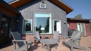 Una cabaña de madera con un porche, dos sillas Adirondack, una mesita y una parrilla cubierta.