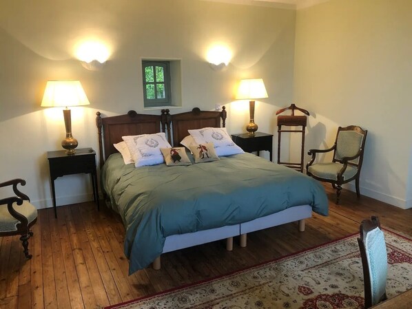 A bedroom with a wooden bed, two bedside tables with lamps, a chair, and a small window.