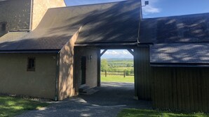 A building with a large open entrance, a gravel driveway, and a view of a green landscape. - 19th century residence - Alpes Mancelles (Rouessé-Vassé)