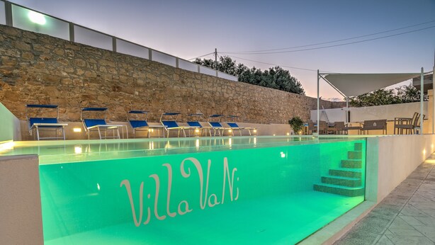 A swimming pool with lounge chairs and a stone wall.