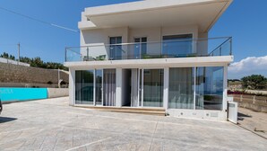 A modern two-story building with a balcony, large glass doors, and a stone wall in the background.