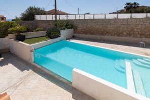 Ein rechteckiger Pool mit Steinmauer und Blumentöpfen darum.