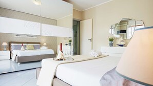 A modern hotel room with a large bed, a separate seating area, a vanity with a mirror, and a small table with a vase of flowers.