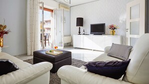 A living room with a sofa, ottoman, TV, and a vase with flowers.