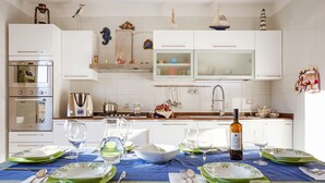A modern kitchen with white cabinets, a built-in oven, and a dining area set for a meal with green plates and wine glasses.