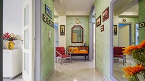 A hallway with a mirror, a red chair, a vanity with a mirror, and a vase with flowers.