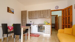 Une cuisine de taille réduite avec des meubles en bois, une table à manger avec des chaises, un canapé et une horloge au mur.