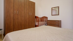 Une chambre avec une grande armoire, un berceau, une commode et un miroir au mur.