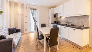 A modern kitchen with white cabinets, a dining table with chairs, a sofa, and a cross on the wall. - Holiday Apartment 'New Casa Ilaria' near Center with Garden & Wi-Fi (Torri del Benaco)