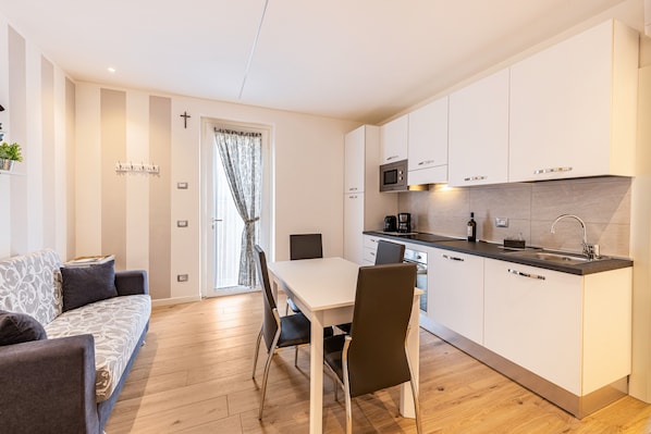 A modern kitchen with white cabinets, a dining table with chairs, a sofa, and a cross on the wall.