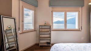 Een slaapkamer met een bed, een plank met schoenen, een ladder en een raam met uitzicht op de zee en bergen.