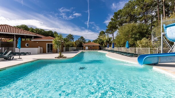 Una piscina con tobogán, sillas de descanso y una zona cubierta con sombrillas.