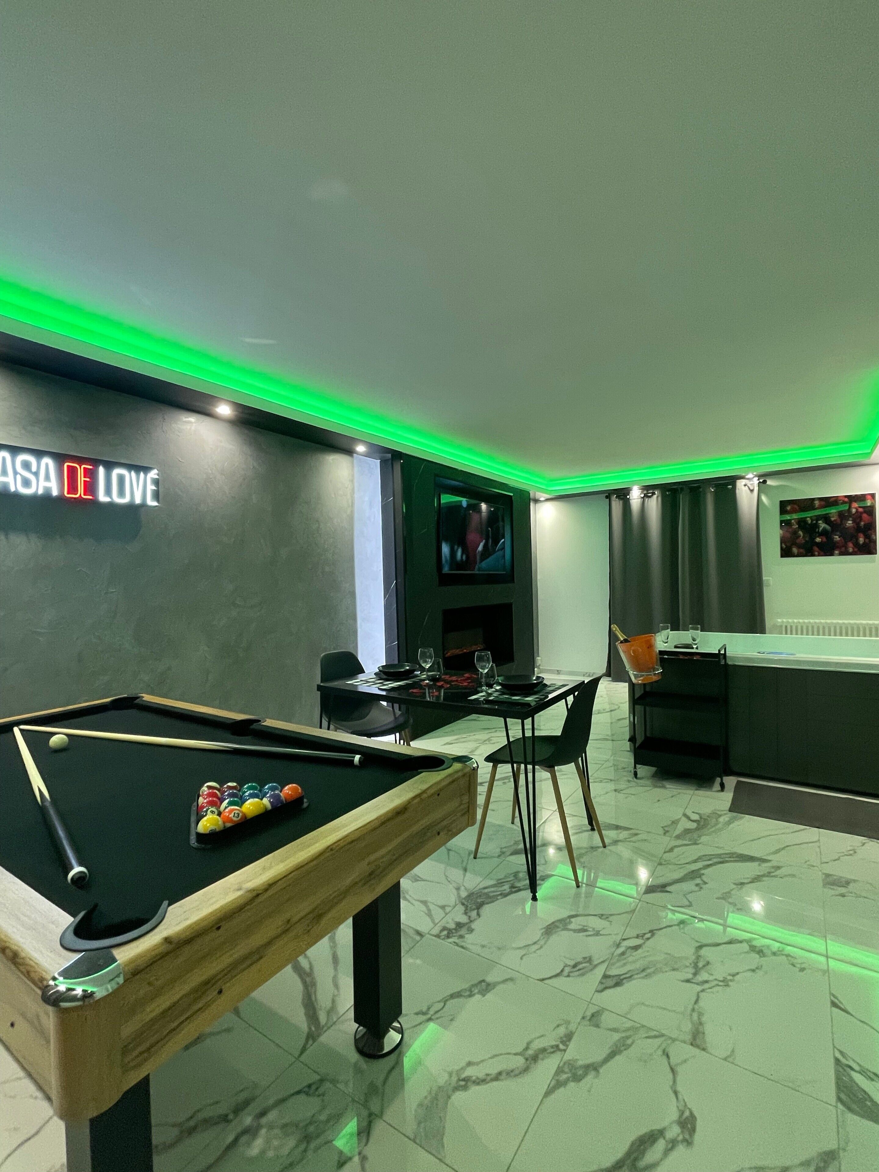 Una mesa de billar, un comedor con sillas, una zona de bar y un televisor montado en la pared.