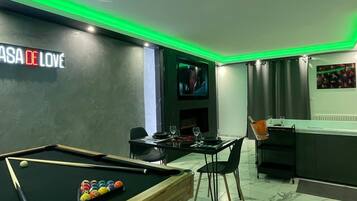 Una mesa de billar, un comedor con sillas, una zona de bar y un televisor montado en la pared.