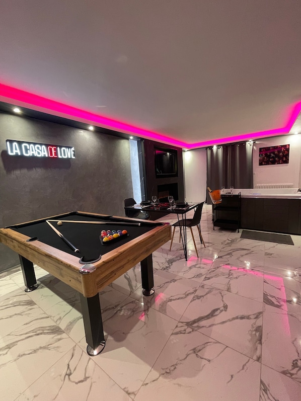 Une table de billard avec un néon, un coin bar et un espace salon.