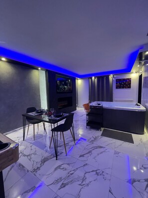 A modern room with a dining table, chairs, a TV, a hot tub, and a fireplace.