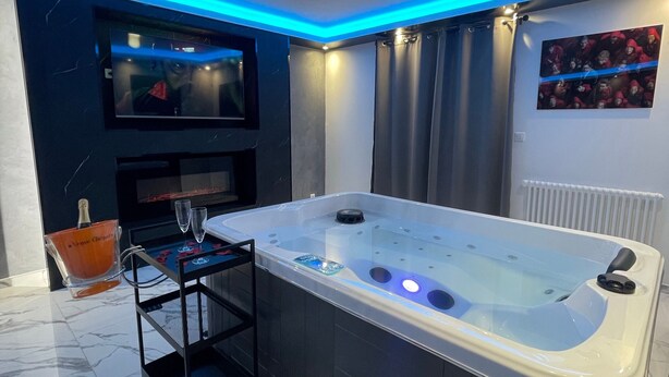 A modern bathroom with a large bathtub, a TV mounted on the wall, and a glass bucket with a bottle. - Holiday Home 'La Casa De Lové Suite Jacuzzi' with Private Garden and Wi-Fi (Melun)