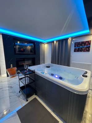 Une salle de bain moderne avec une grande baignoire, un téléviseur fixé au mur et un seau en verre contenant une bouteille.