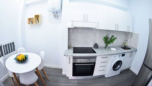 Una cocina compacta con armarios blancos, horno empotrado, lavadora y comedor con mesa y sillas.