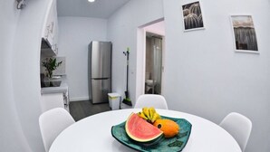 Una cocina moderna con armarios blancos, un refrigerador de acero inoxidable y una zona de comedor con una mesa redonda.