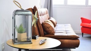 Una sala de estar moderna con un sofá de cuero marrón, una mesa redonda de madera con cubierta de vidrio, una lámpara de metal y una silla roja.