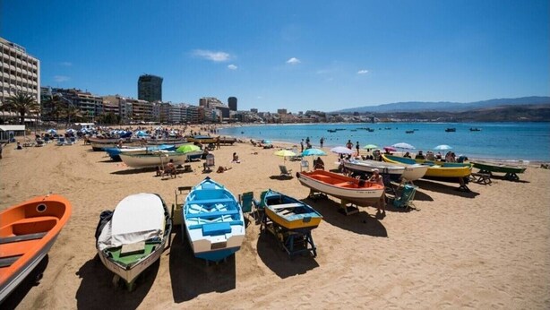 Una playa con barcos, sombrillas y gente.
