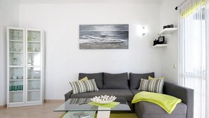 Een woonkamer met een glazen salontafel, een grijze bank en een schilderij van de oceaan.
