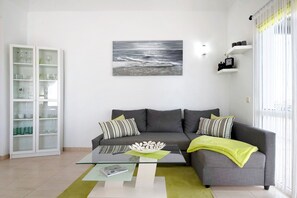 A living room with a glass coffee table, grey sofa, and a painting of the ocean.