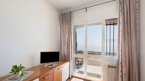 A room with a wooden desk, a television, a potted plant, and a sliding glass door leading to an outdoor area. - Apartment "Oleandro" with Sea View, Garden & Wi-Fi (Finale Ligure)