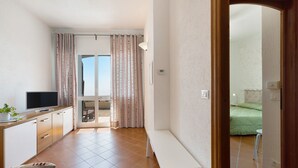 A modern room with a TV, a bench, a dining area, and a view through a door. - Apartment "Oleandro" with Sea View, Garden & Wi-Fi (Finale Ligure)