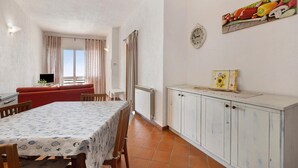 A dining area with a table set for two, a red sofa, a white cabinet, and a wall clock. - Apartment "Oleandro" with Sea View, Garden & Wi-Fi (Finale Ligure)
