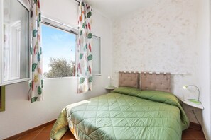 Un dormitorio con cama, ventana con cortinas, mesita de noche con lámpara y pared con textura.