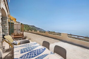 A terrace with a table and chairs, a wooden bench, and a view of the sea.