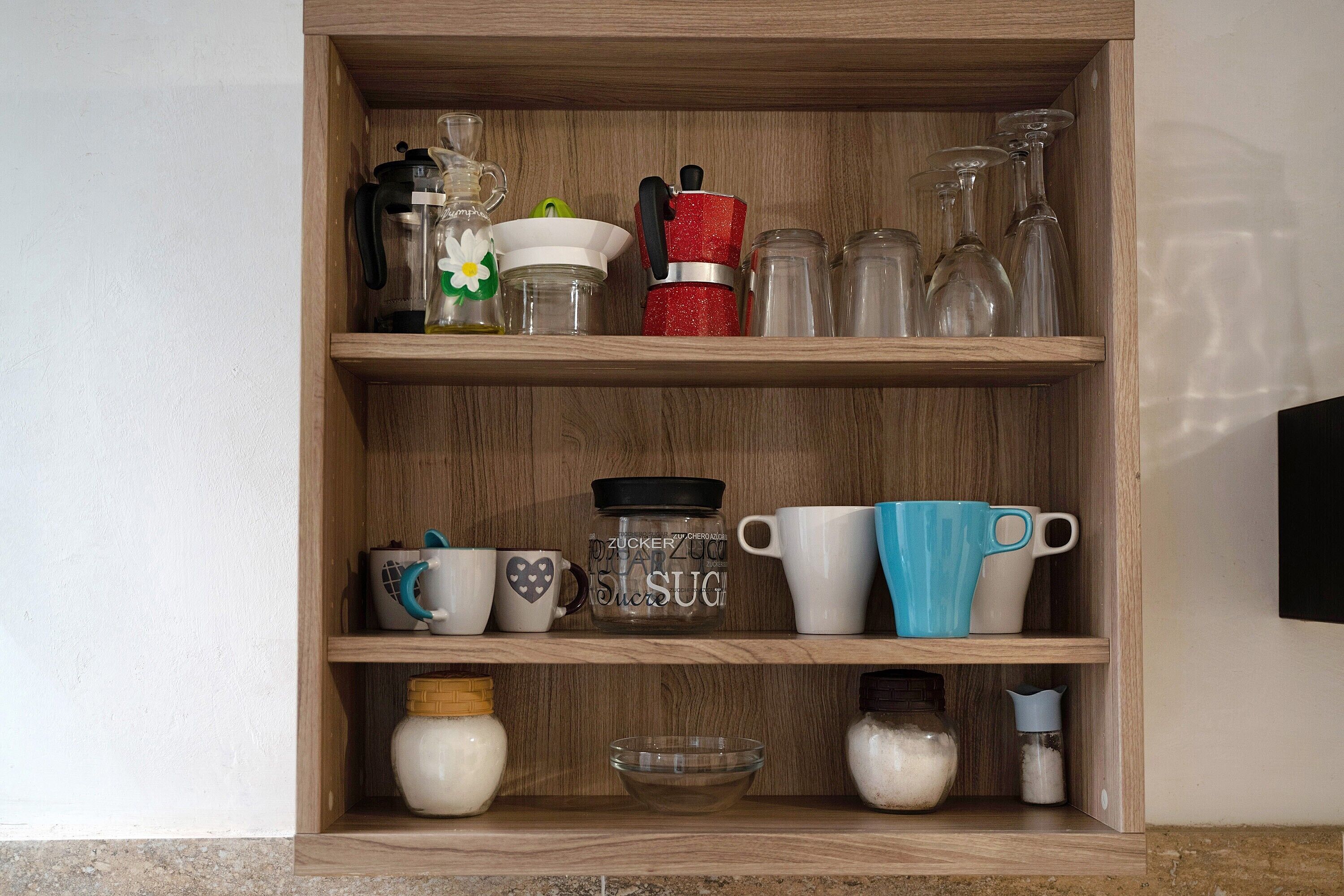 A wooden shelf with various kitchen items including a coffee maker, mugs, and jars.