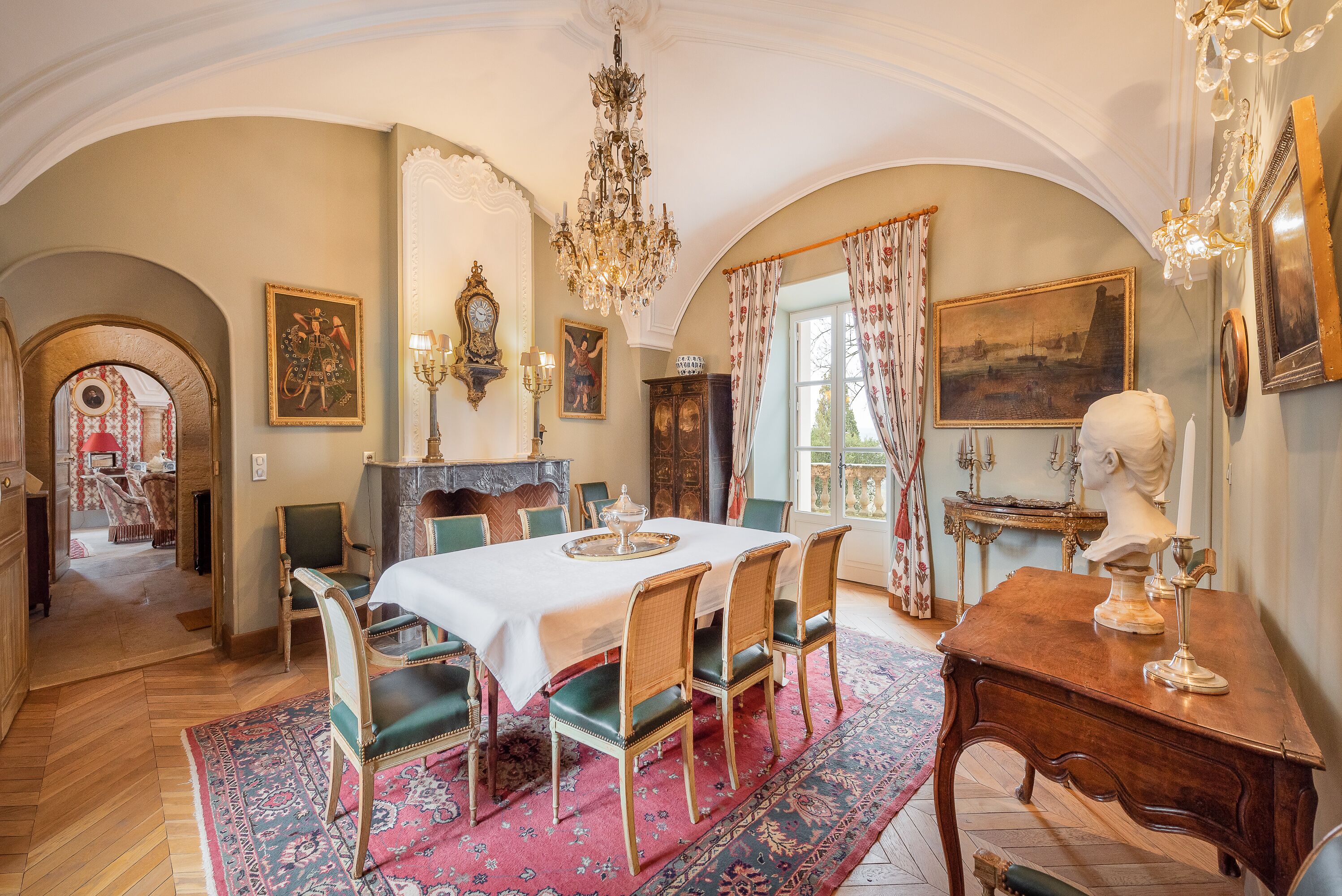 Comedor con candelabro, una mesa dispuesta para cuatro personas y un cuadro grande en la pared.