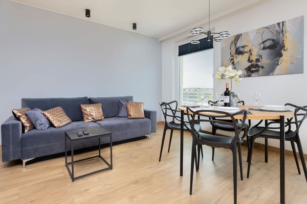A modern living room with a comfortable sofa and stylish coffee table, complemented by contemporary decor on the walls. Large windows bring in natural light, creating an inviting space.