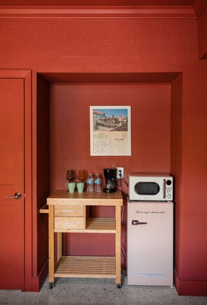 Une petite cuisine équipée avec un bureau en bois, un réfrigérateur de style rétro et une carte postale encadrée accrochée au mur.