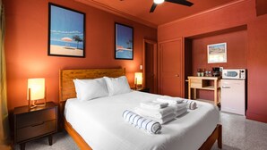 Une chambre d’hôtel comprenant un lit, des tables de chevet, un ventilateur de plafond, un bureau avec un micro-ondes et une porte donnant sur une autre pièce.