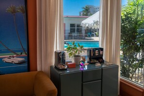 A room with a view of a swimming pool, a potted plant, and a desk with a toaster and books.