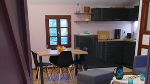 Una cocina moderna con armarios oscuros, una mesa de comedor de madera y una pequeña zona de estar con un otomano gris.